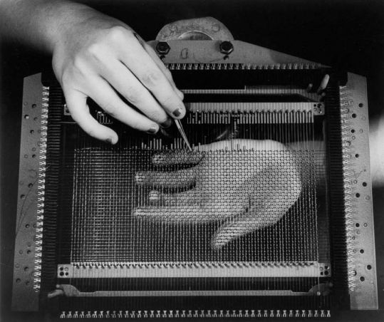 A hand holding an instrument over a weaving mesh an another hand underneath.