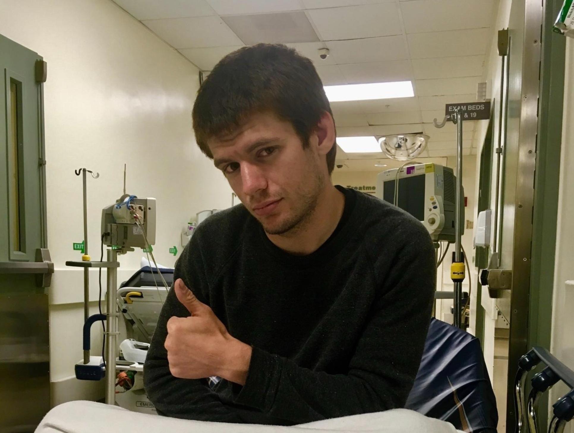 Andy sitting on a hospital bed and giving a thumbs up