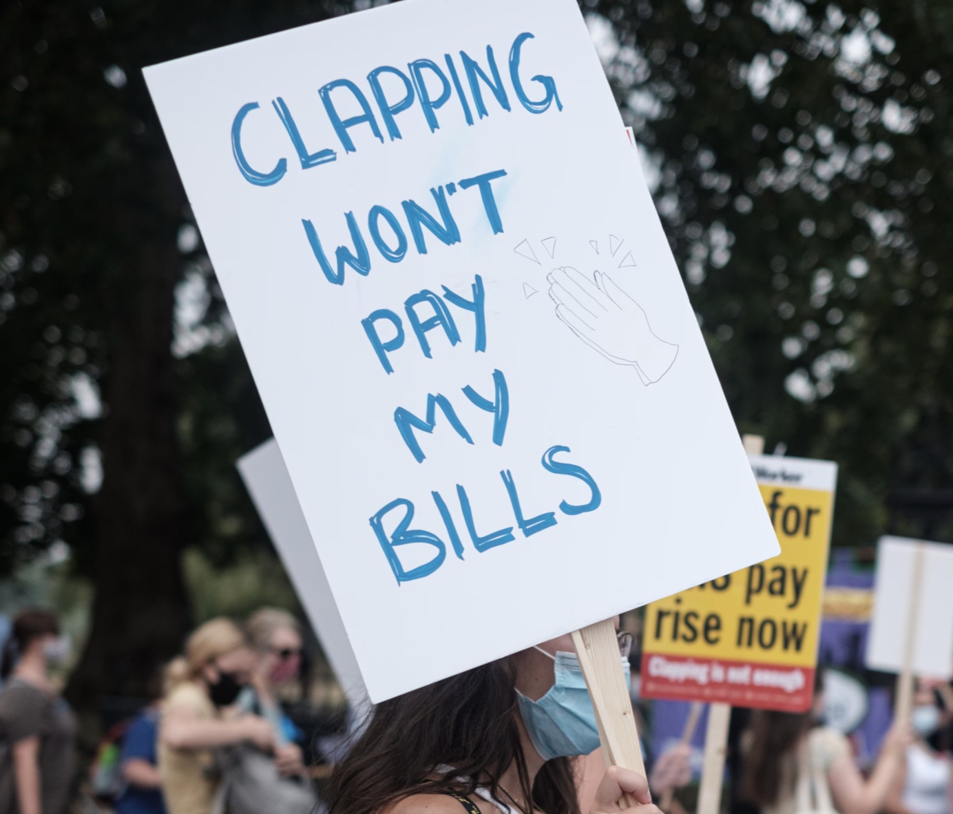 A person holding a sign that says CLAPPING WON'T PAY MY BILLS