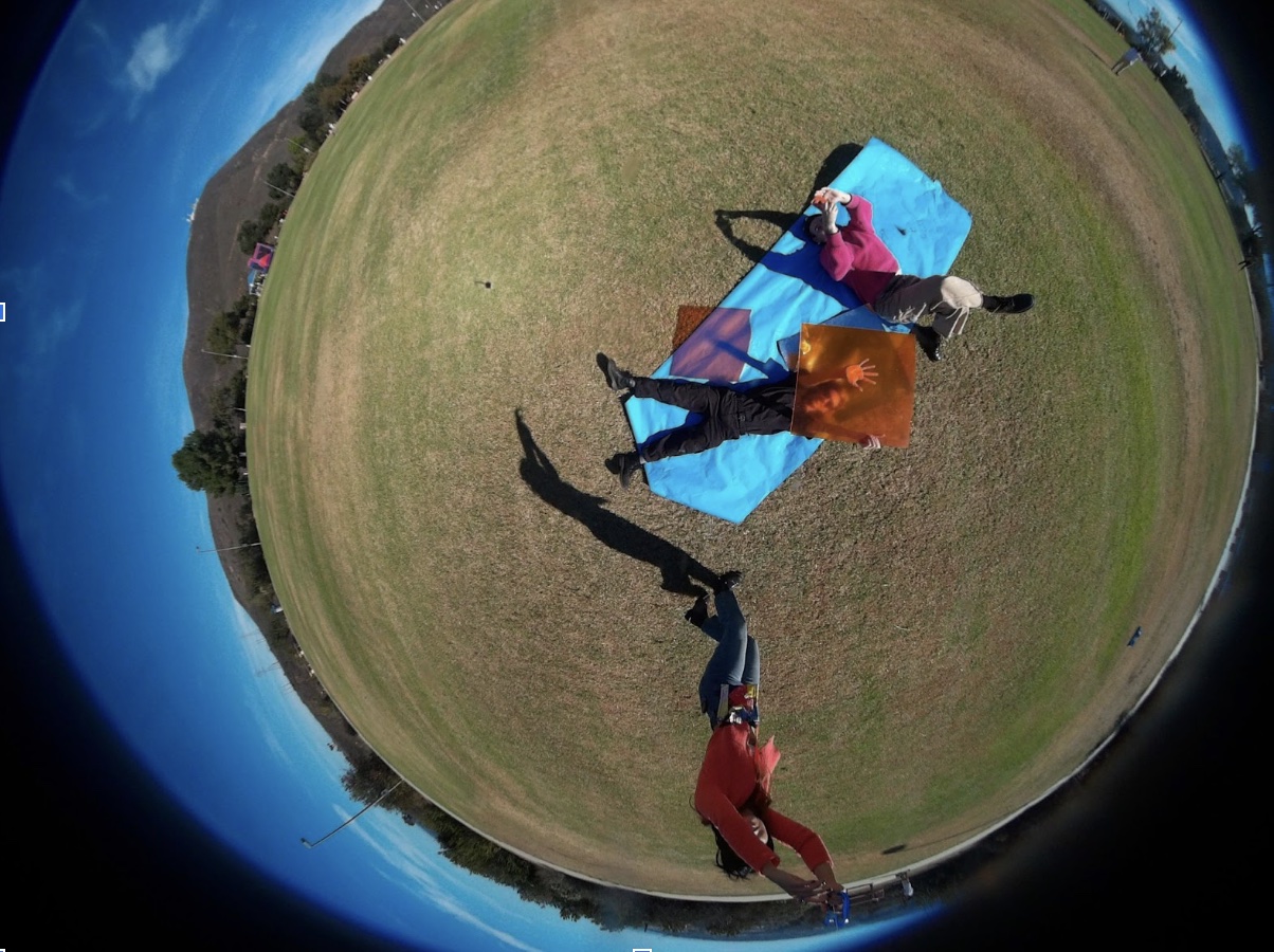 One person holds the string of the kite, while another holds an orange filter over their face, and a third takes the photograph using a phone app connected to the kite camera.