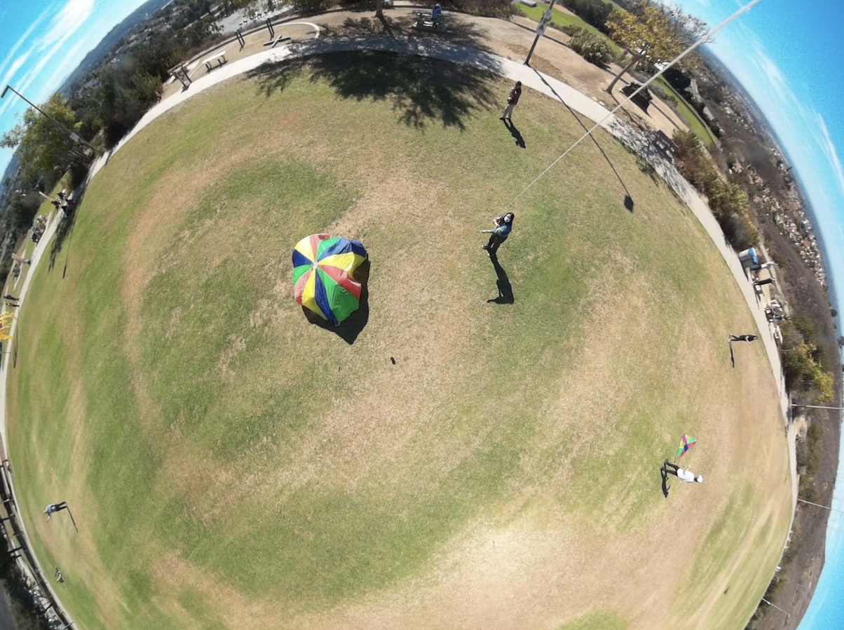 A group becomes invisible to the camera by huddling under a colored parachute.