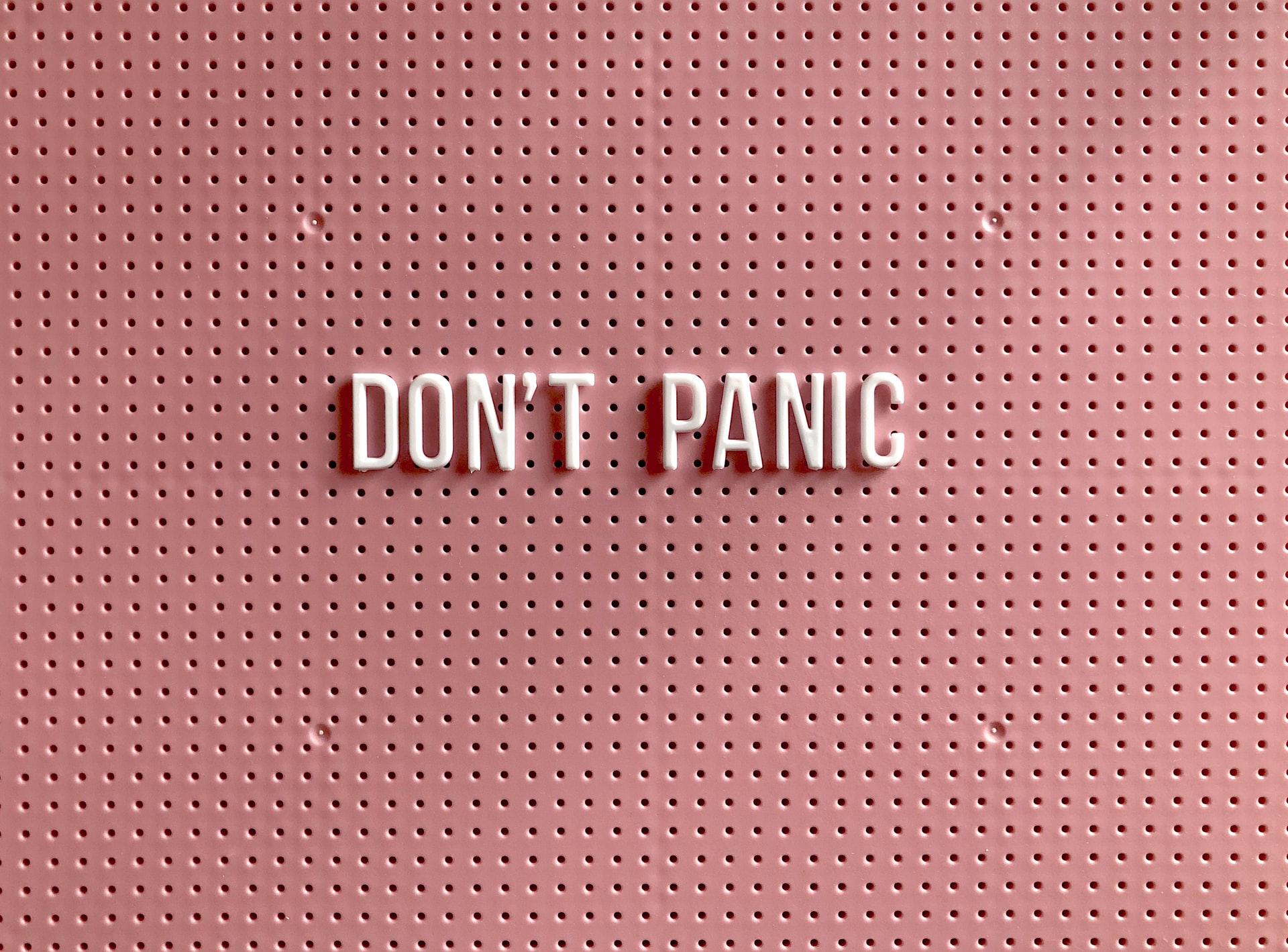 White letters on a board colored millennial pink that say DON'T PANIC