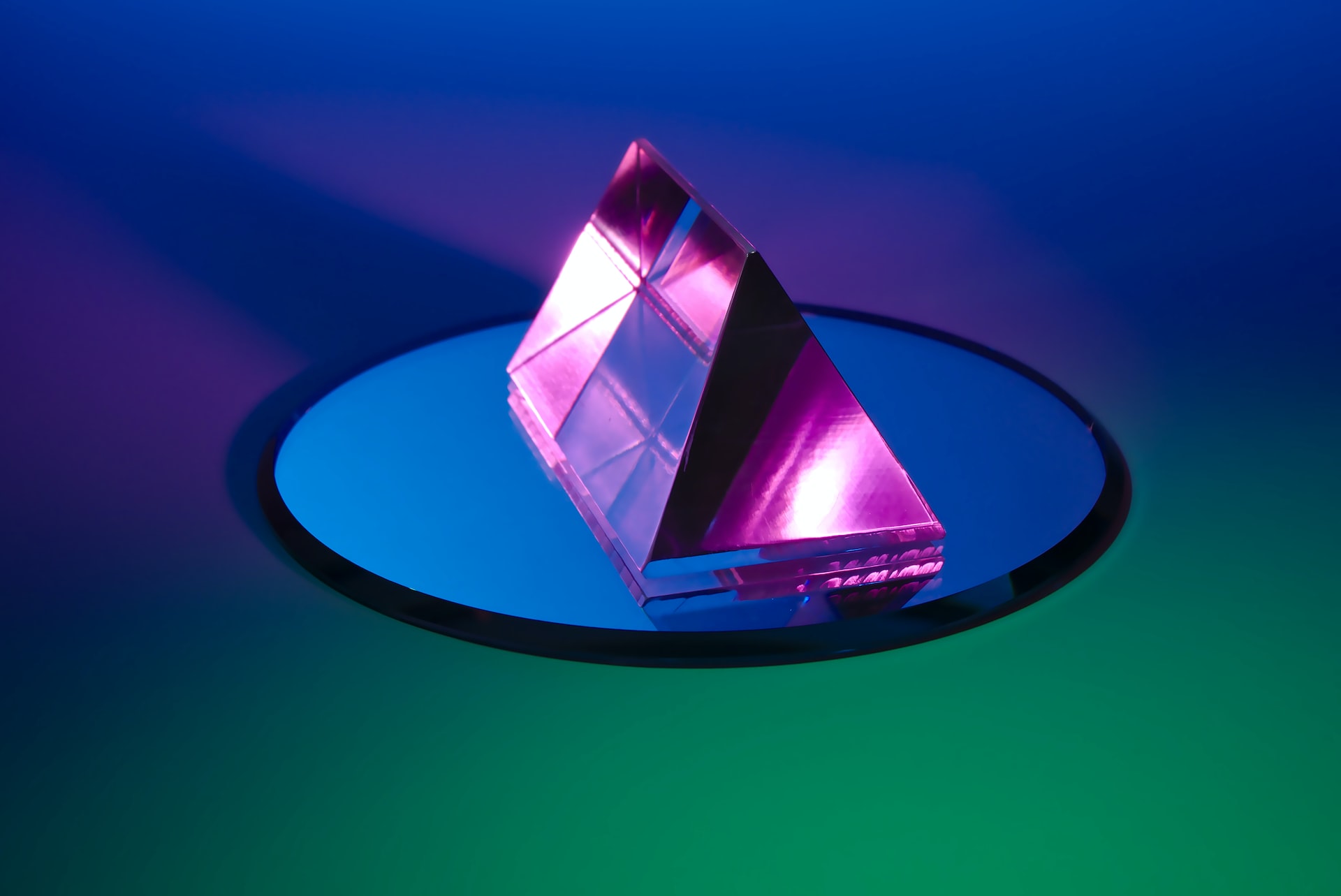A neon pink prism on round blue mirror with a blue and green gradient background