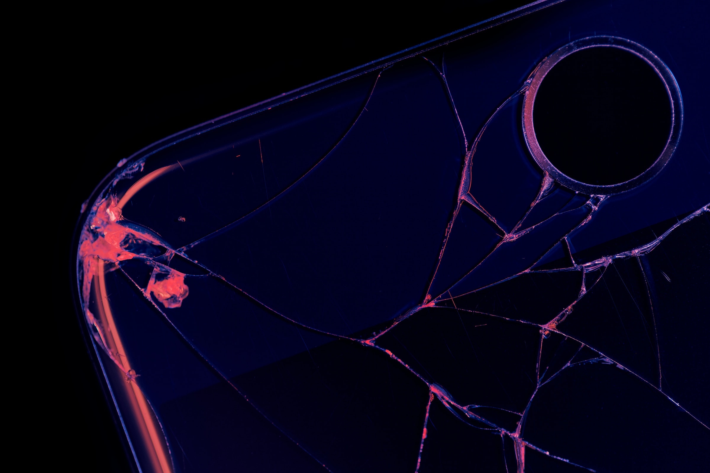 A close-up image of a cracked phone showing the camera lense, in black and neon pink and purple